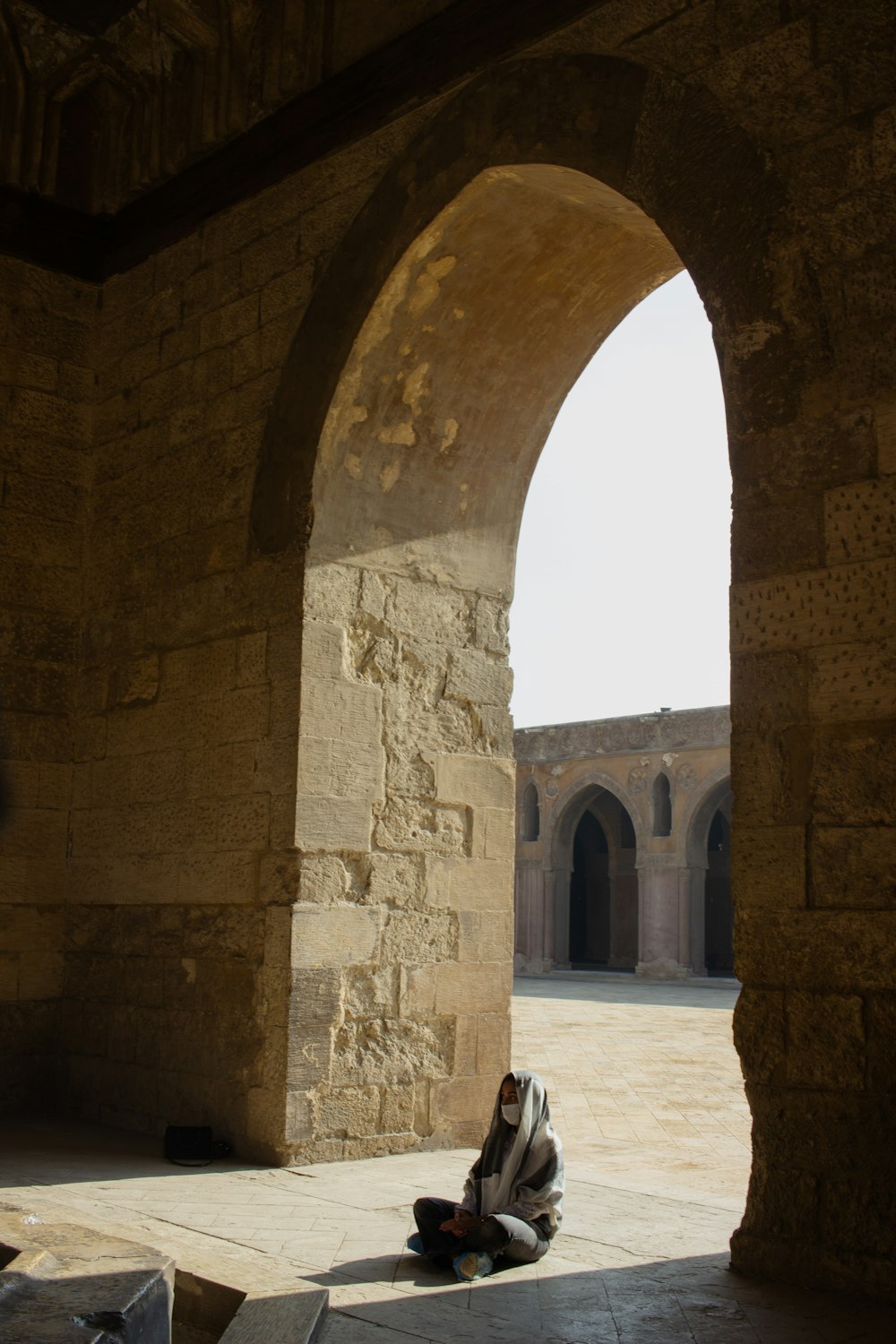 a person sitting on the ground under an arch