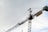 A large construction crane is captured against a cloudy sky. The crane is built with a lattice framework and features a prominent yellow sign with the word 'Azvi' on it.