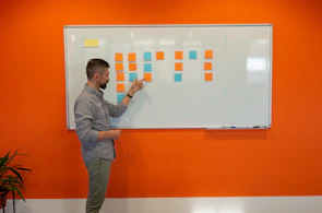 A smiling instructor explaining budgeting concepts with colorful charts on a whiteboard.