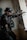 A tactical soldier dressed in full gear and helmet is aiming a rifle while standing indoors against a wall with graffiti. The soldier wears sunglasses and has various tactical equipment attached to their vest. The setting appears to be an urban, possibly abandoned structure.