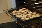 A baking tray filled with golden brown crackers is placed inside an oven. The crackers have a light dusting of what seems to be salt or cheese on their surface.