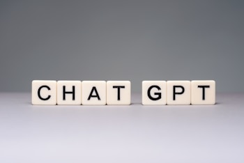 Blocks with letters spell out 'CHAT GPT' on a smooth surface. The blocks are light-colored with black letters, arranged in two groups.