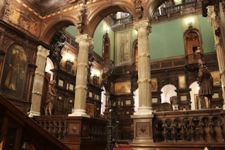 An ornately decorated interior with tall pillars, intricate wood carvings, and classical Renaissance artwork. The space is illuminated by warm lighting, highlighting the opulent architectural details and statues positioned throughout the room.