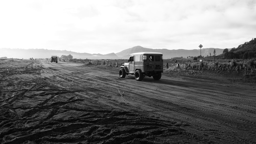 a black and white photo of a truck driving down a dirt road