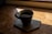 Close-up of a steaming cup of freshly brewed coffee on a wooden table with sunlight filtering through a window.