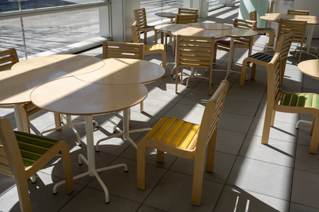 A sunlit common room with colorful cushions and travelers chatting around a wooden table.