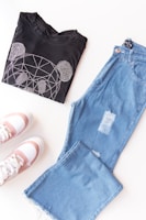 A casual outfit laid out on a wooden bench featuring a black jacket with rose gold buttons and matching joggers.