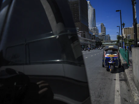A sleek tuk tuk parked near a sunlit Lisbon viewpoint with the cityscape in the background.