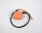 An orange ignition coil with a pair of mounting brackets and a black wire attached. The coil is cylindrical and flanked by two flat metal pieces with circular holes for securing it. The wire is partially coiled with both ends exposed, visible on a plain white background.