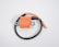 An orange ignition coil with a pair of mounting brackets and a black wire attached. The coil is cylindrical and flanked by two flat metal pieces with circular holes for securing it. The wire is partially coiled with both ends exposed, visible on a plain white background.