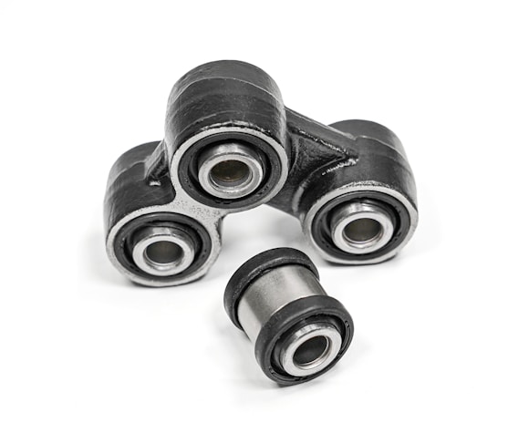 A close-up of metal mechanical components consisting of multiple rubber bushings. The bushings are primarily black with a metallic silver inner ring and are set against a plain white background.