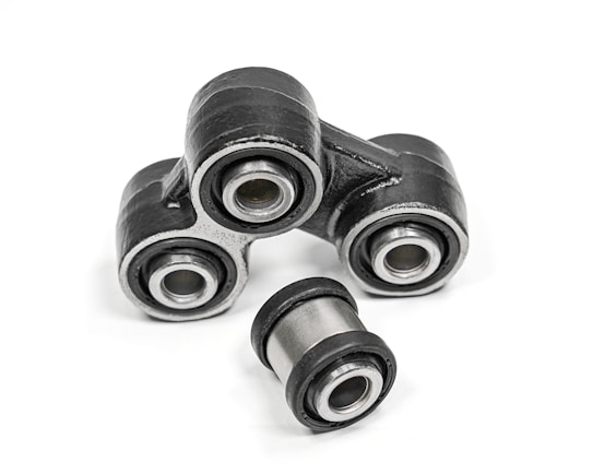 A close-up of metal mechanical components consisting of multiple rubber bushings. The bushings are primarily black with a metallic silver inner ring and are set against a plain white background.