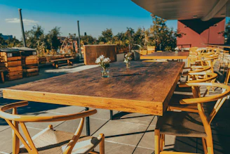 Elegant solid wood patio dining table set with matching chairs under a bright blue sky.