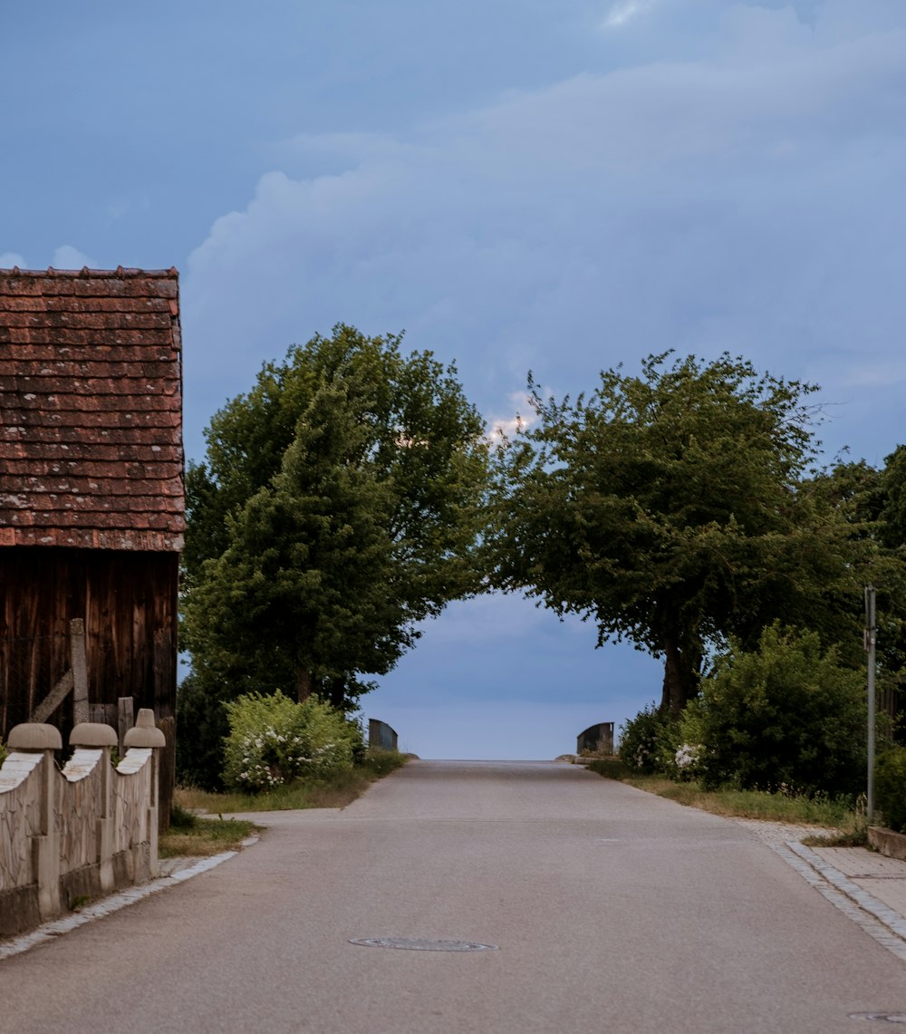 an empty road with a barn and trees on either side