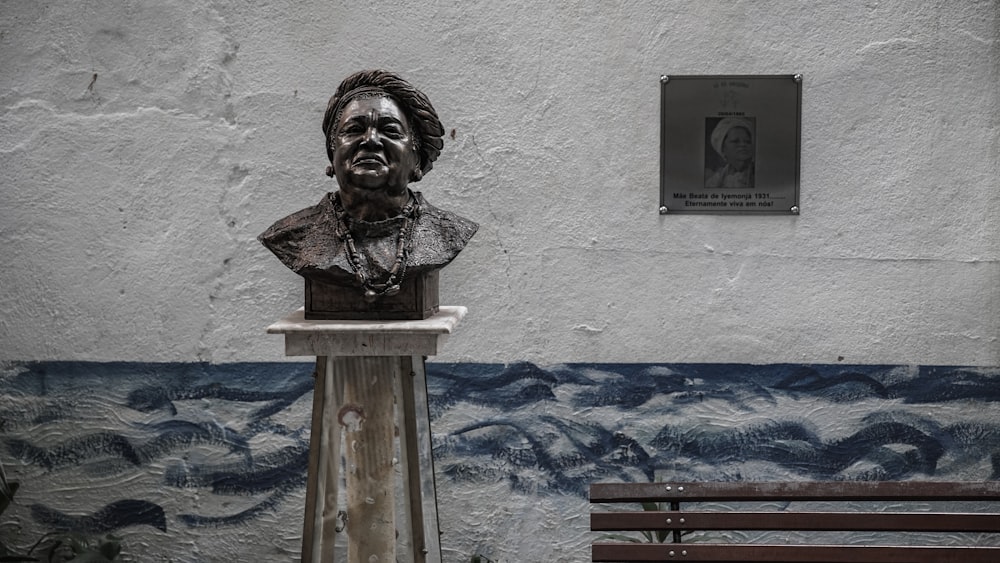 a busturine of a man sitting on a bench in front of a wall