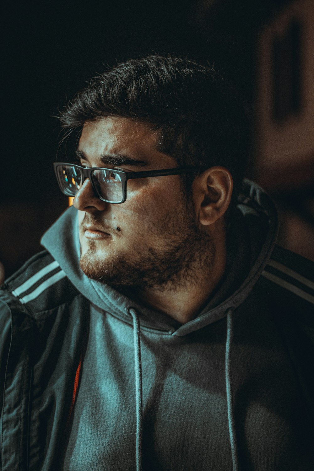 a man wearing glasses and a hoodie looks off into the distance