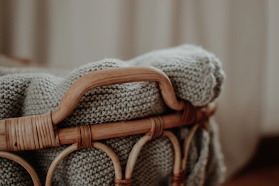 A decorative woven basket filled with soft blankets on a warm hardwood floor.