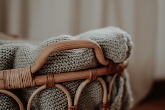 A textured, knit blanket is draped over the edge of a wicker basket. The scene is softly lit, creating a warm and cozy atmosphere.