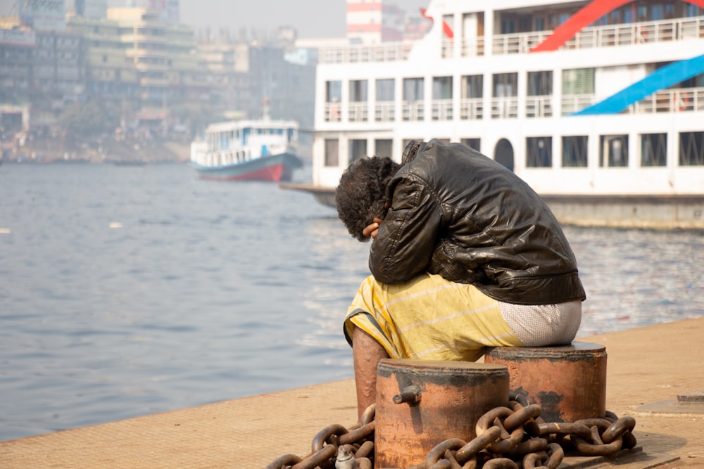 a man sitting on a bucket next to a body of water