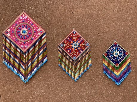 Colorful decorative wall hangings crafted by local artisans displayed on a textured wall.