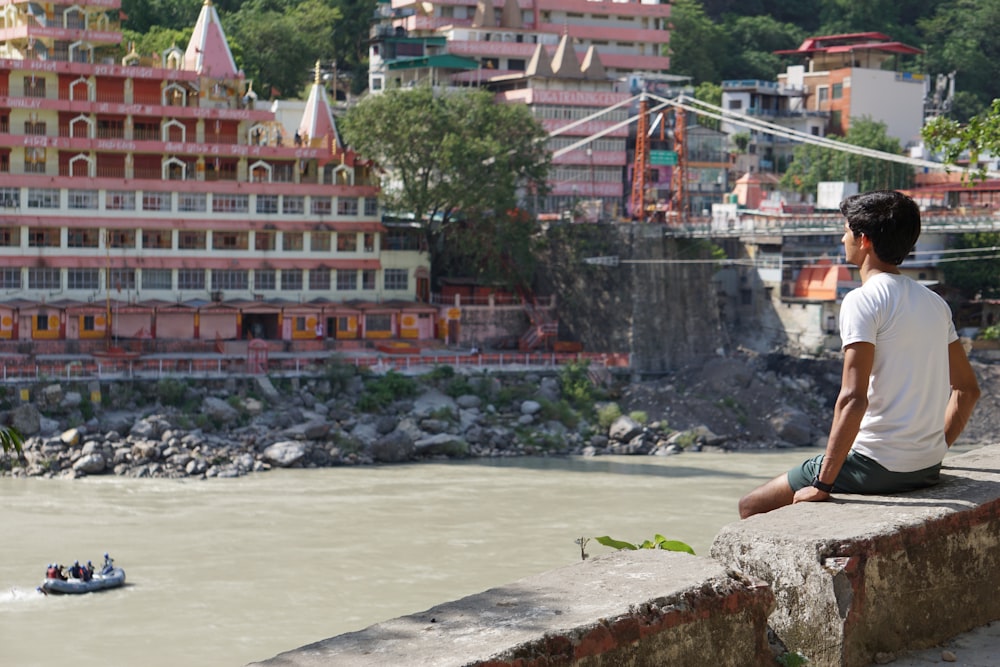 a man sitting on a ledge looking out over a river