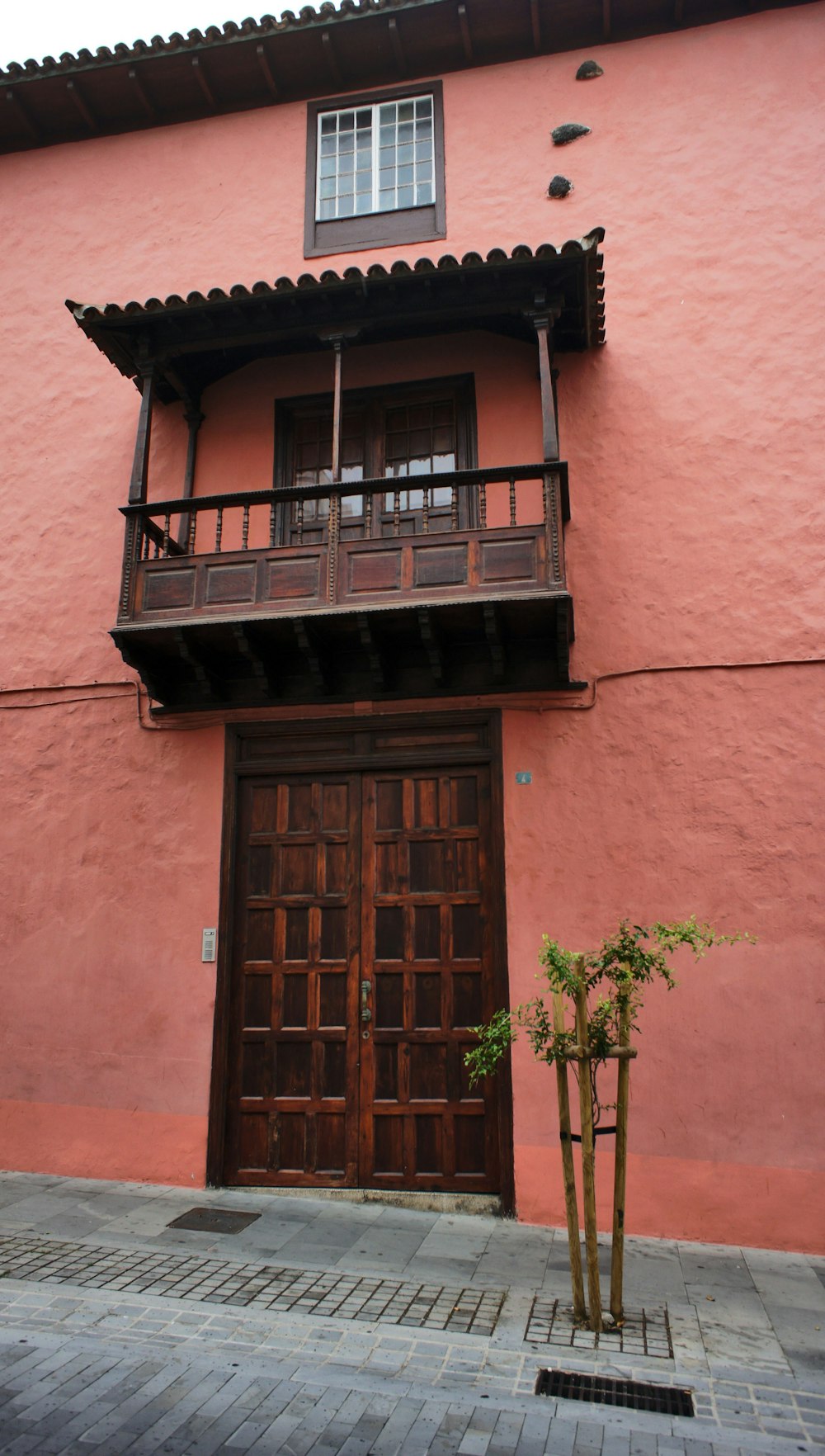 a tall pink building with a wooden door and balcony