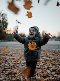 A close-up of a child laughing amidst falling leaves, showcasing the joy of family time in nature.