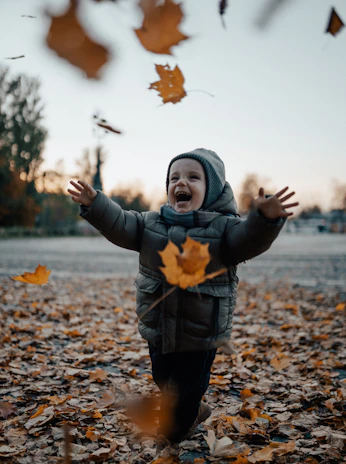A slow-motion capture of autumn leaves drifting down around a laughing child in a knitted sweater.