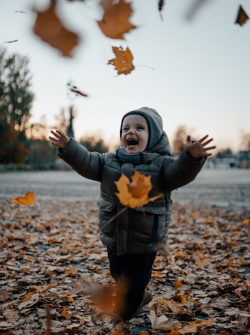 A close-up of a child laughing amidst falling leaves, showcasing the joy of family time in nature.