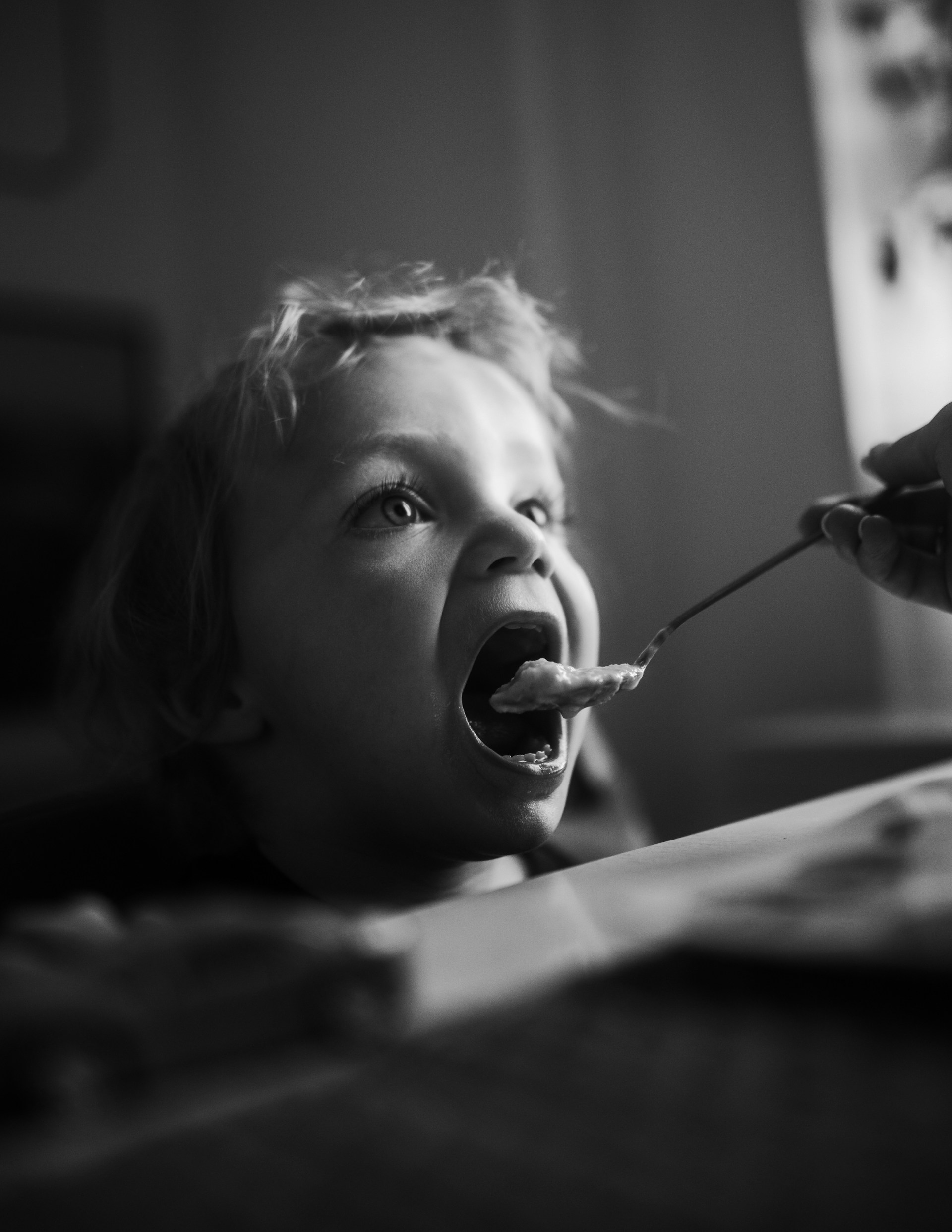 a little boy that is sitting down with a spoon in his mouth