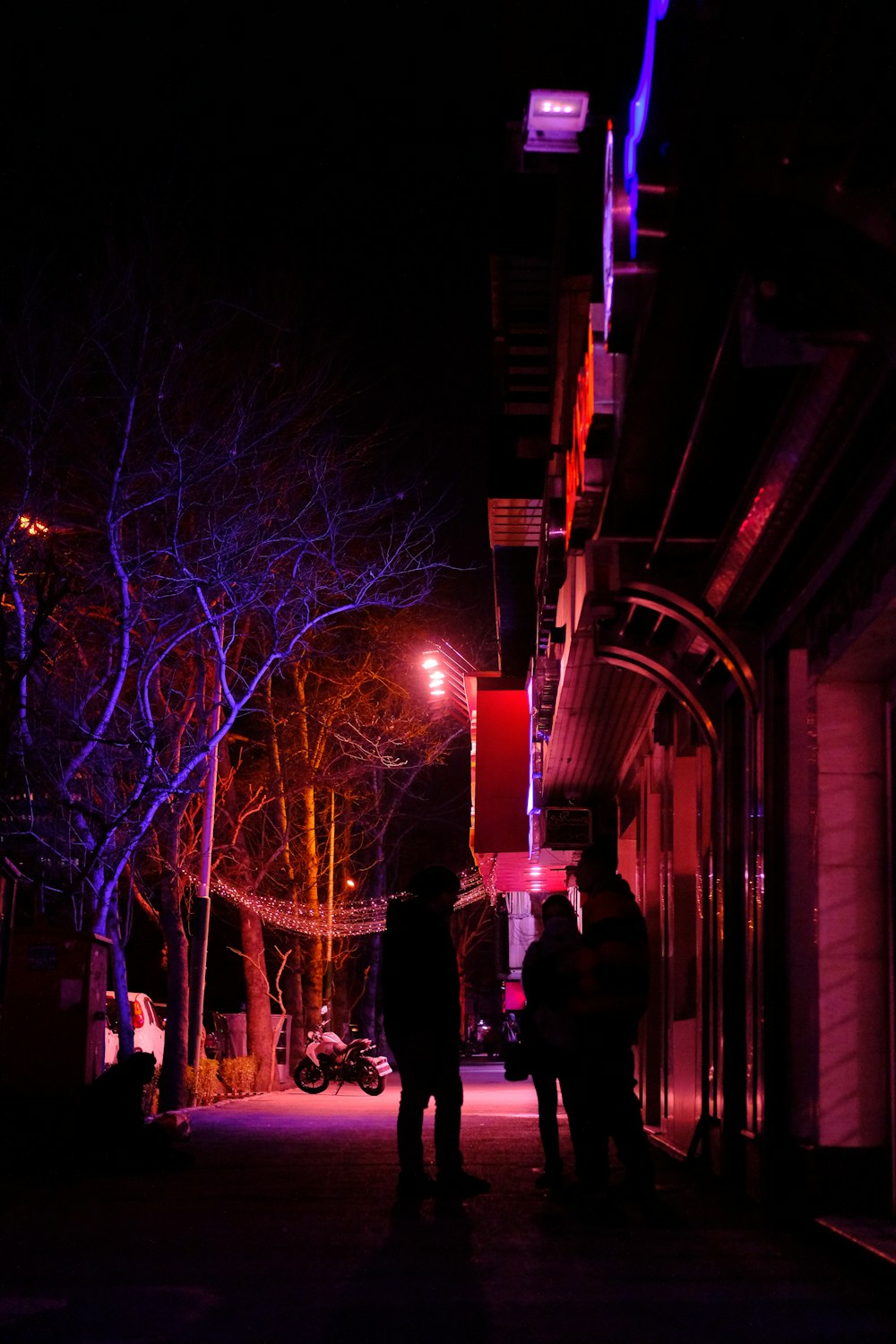 a couple of people standing on a sidewalk at night