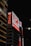 Large illuminated billboards with Japanese characters are displayed on the side of a tall building at night. Bright red and white lights are prominent with a dark sky backdrop, creating a vibrant contrast.