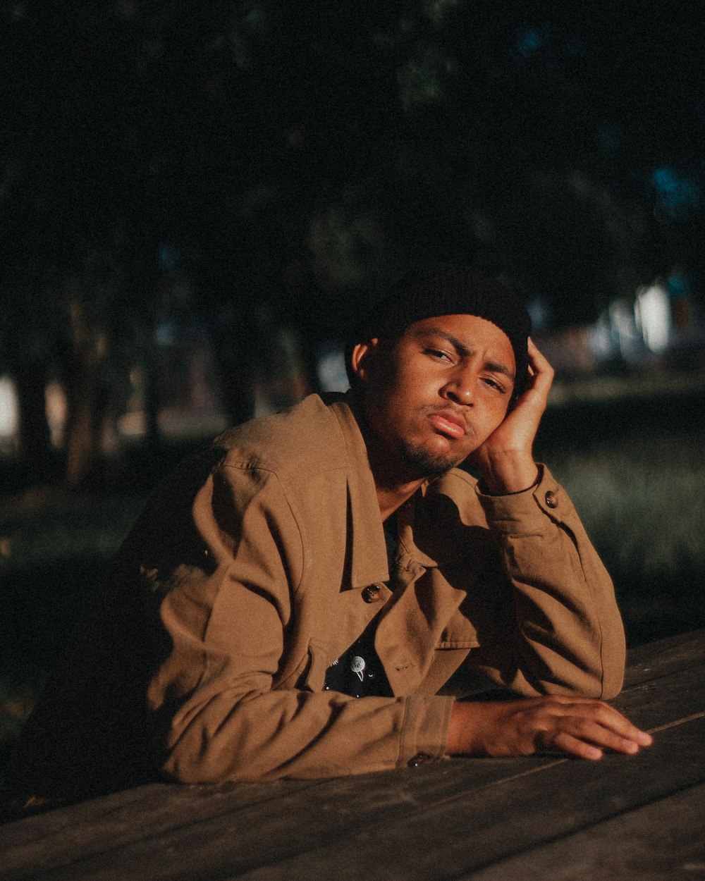 a man in a trench coat sitting on a wooden bench