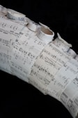 A collage made of several sheets of paper with musical notation and sheet music arranged in a layered and overlapping fashion. Some of the sheets are rolled or curled, giving a three-dimensional texture to the artwork.