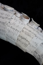 A collage made of several sheets of paper with musical notation and sheet music arranged in a layered and overlapping fashion. Some of the sheets are rolled or curled, giving a three-dimensional texture to the artwork.