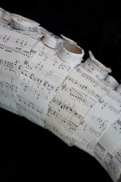 A collage made of several sheets of paper with musical notation and sheet music arranged in a layered and overlapping fashion. Some of the sheets are rolled or curled, giving a three-dimensional texture to the artwork.
