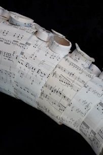 A collage made of several sheets of paper with musical notation and sheet music arranged in a layered and overlapping fashion. Some of the sheets are rolled or curled, giving a three-dimensional texture to the artwork.