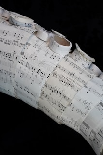 A collage made of several sheets of paper with musical notation and sheet music arranged in a layered and overlapping fashion. Some of the sheets are rolled or curled, giving a three-dimensional texture to the artwork.
