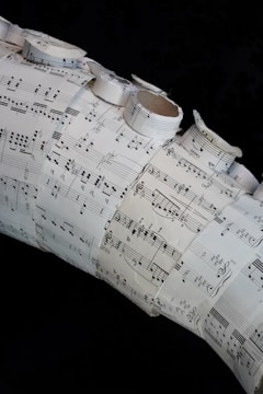 A collage made of several sheets of paper with musical notation and sheet music arranged in a layered and overlapping fashion. Some of the sheets are rolled or curled, giving a three-dimensional texture to the artwork.