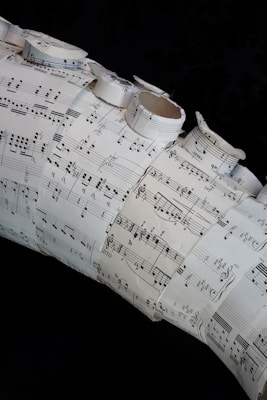 A collage made of several sheets of paper with musical notation and sheet music arranged in a layered and overlapping fashion. Some of the sheets are rolled or curled, giving a three-dimensional texture to the artwork.
