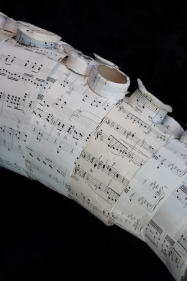 A collage made of several sheets of paper with musical notation and sheet music arranged in a layered and overlapping fashion. Some of the sheets are rolled or curled, giving a three-dimensional texture to the artwork.