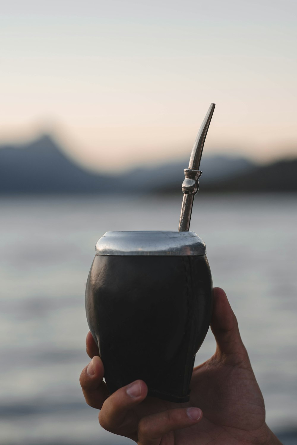 a person holding a drink in their hand near a body of water