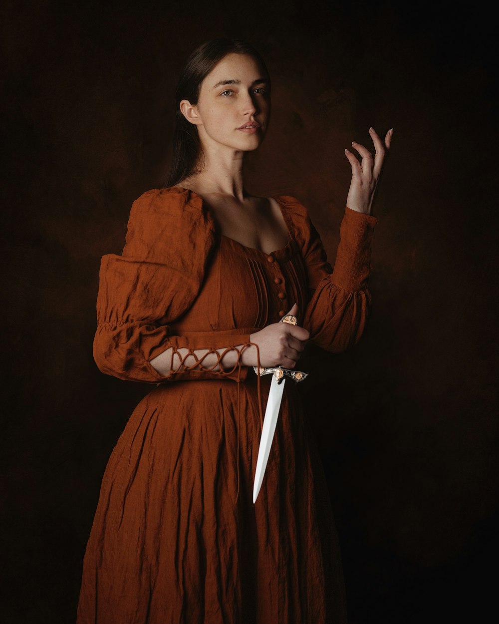 Una mujer con un vestido marrón sosteniendo un cuchillo