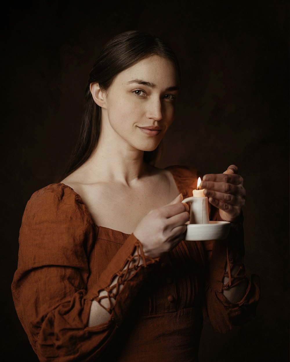 Eine Frau in einem braunen Kleid, die eine Kerze hält