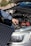 A person is adjusting or inspecting something under the hood of a car, with a focus on the battery and cables. A solar panel is positioned near the car, possibly for charging or testing purposes.
