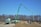 A green construction truck with an extended boom is situated at a construction site with piles of dirt and unfinished structures. Leafless trees are in the background under a clear blue sky.