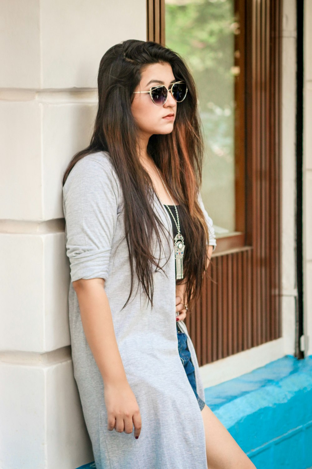 a woman leaning against a wall wearing sunglasses