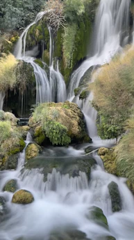 A serene waterfall cascading over moss-covered rocks surrounded by lush greenery.