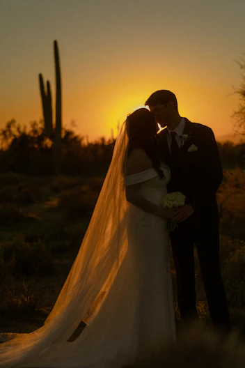 a bride and groom kissing in front of a sunset