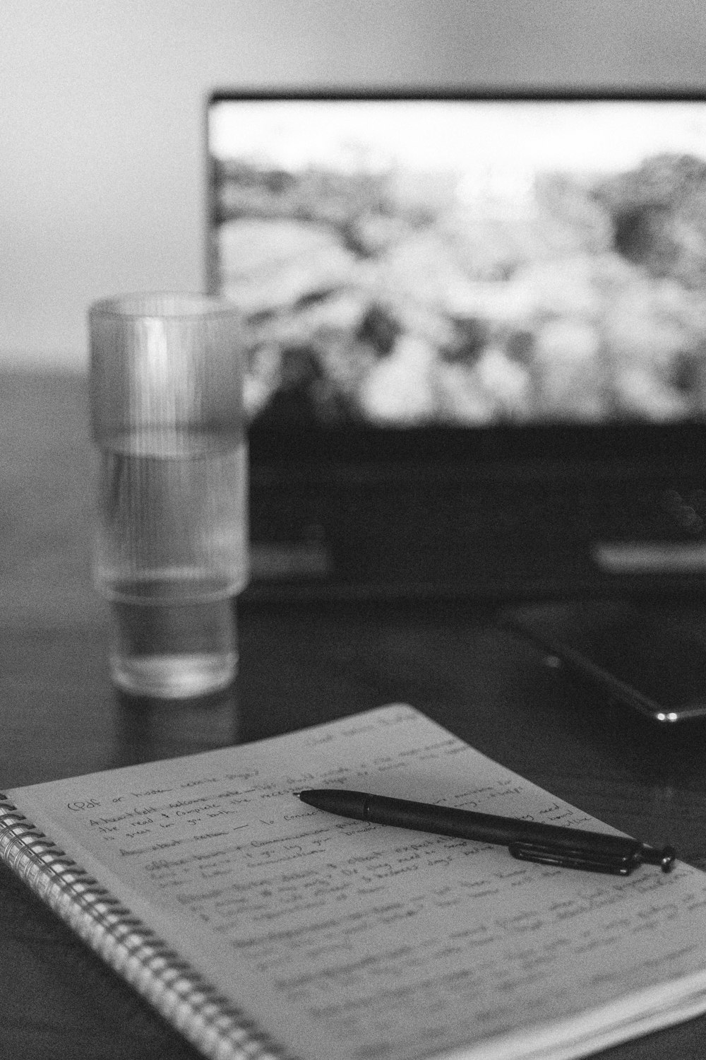 a notebook and a pen on a table with a television in the background